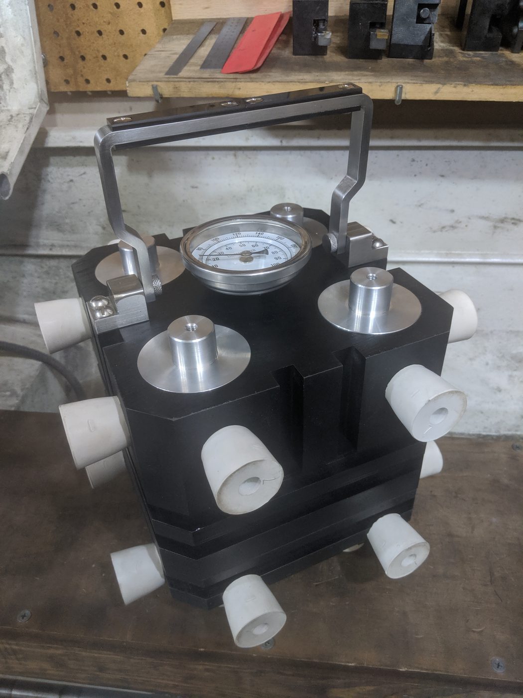 Figure 12 — Three-quarter view of the finished black-crackle replica box with hardware installed. The horizontal cooling fins are visible on all four side faces; the urchin port plugs, thermometer, and aluminu…